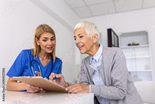 фотографія Smiling female doctor holding a clipboard while a happy senior patient signs a medical consent form or insurance document during a clinical visit