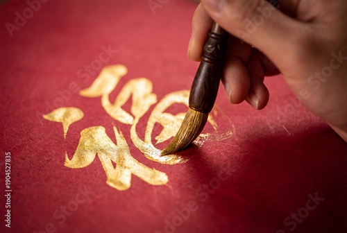 Hand writing chinese calligraphy character fu with golden ink on red paper during lunar new year