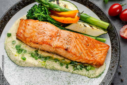 Salmon fillet served with vegetables and sauce on a plate. A salmon fillet is served on a plate with grilled vegetables and a creamy sauce at a restaurant.