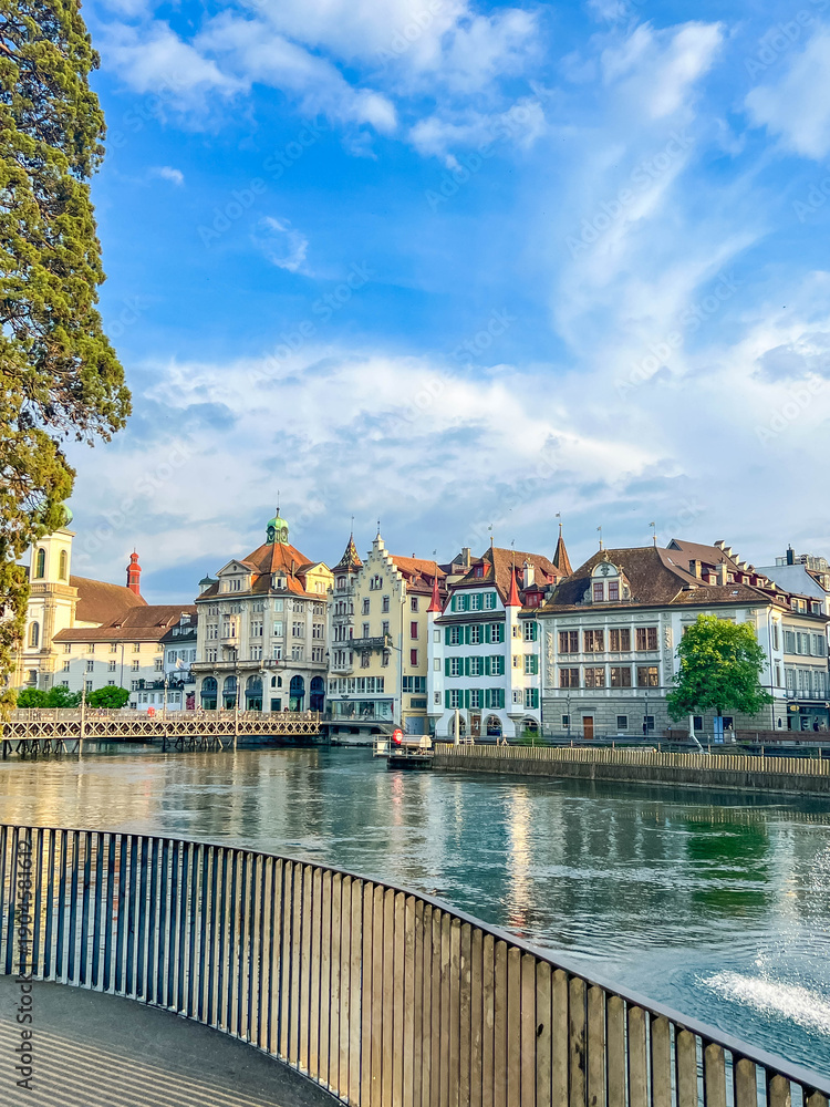 Fototapeta premium Zurich, Switzerland, May 01, 2025. Picturesque riverside walkway with wooden railings overlooking the historic colorful buildings of old town Zurich. High quality photograph.