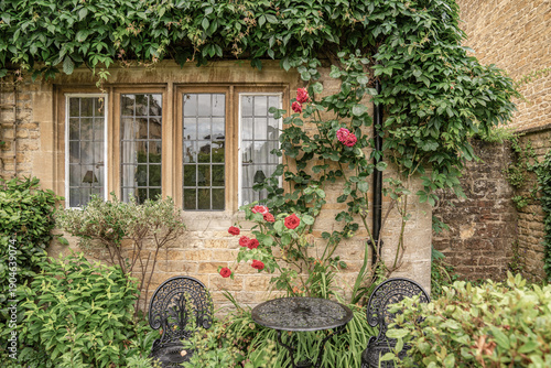 Quadro su tela A charming English country garden corner with climbing roses, classic stone walls, and wrought iron chairs, creating a peaceful outdoor setting