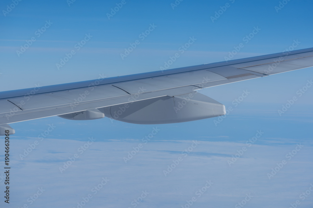 Obraz premium Airplane wing stretches over a soft cloud layer under a clear blue sky, captured mid-flight, highlighting calm travel and high-altitude perspective.