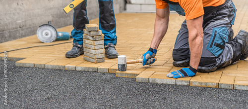 Laying of the interlocking paving. Worker compacting locking blocks in their laying bed using a rubber hammer.