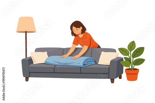 Person folds a blue blanket on a grey couch in a living room with a lamp and a potted plant