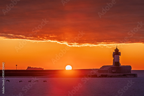 Sonnenaufgang über zugefrorener Ostsee mit Leuchtturm Sassnitz als Silhouette und Frachter am Horizont, Insel Rügen, Mecklenburg-Vorpommern, Deutschland