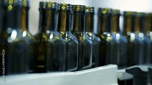Close up of dark glass bottles moving on a conveyor belt during the automated filling and capping process in an industrial olive oil manufacturing plant.