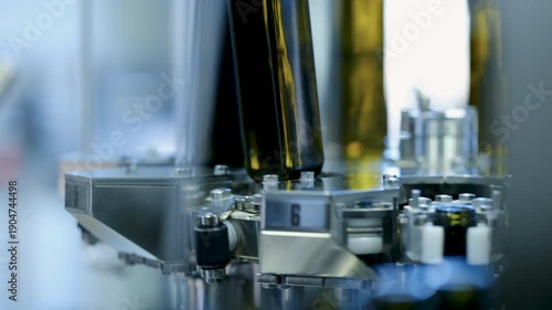 Close up of dark glass bottles moving on a conveyor belt during the automated filling and capping process in an industrial olive oil manufacturing plant.