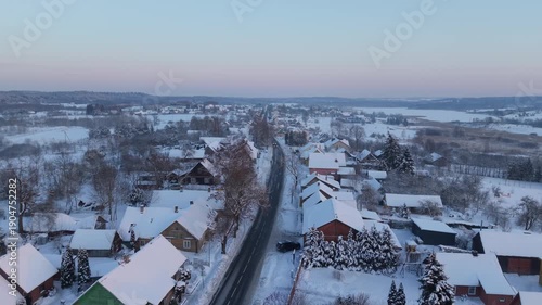 4K aerial drone lateral right establishing shot of Semeliškės near Trakai, Lithuania, winter village street lined with houses and trees at golden hour, cinematic footage