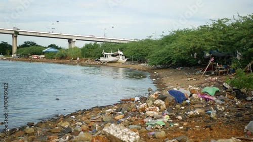 Shoreline trash sea full of plastic waste rubbish and overwhelming abundance garbage, docking or mooring of boat on shore then small temporary shelter house with blue tarps roof liquors on the table