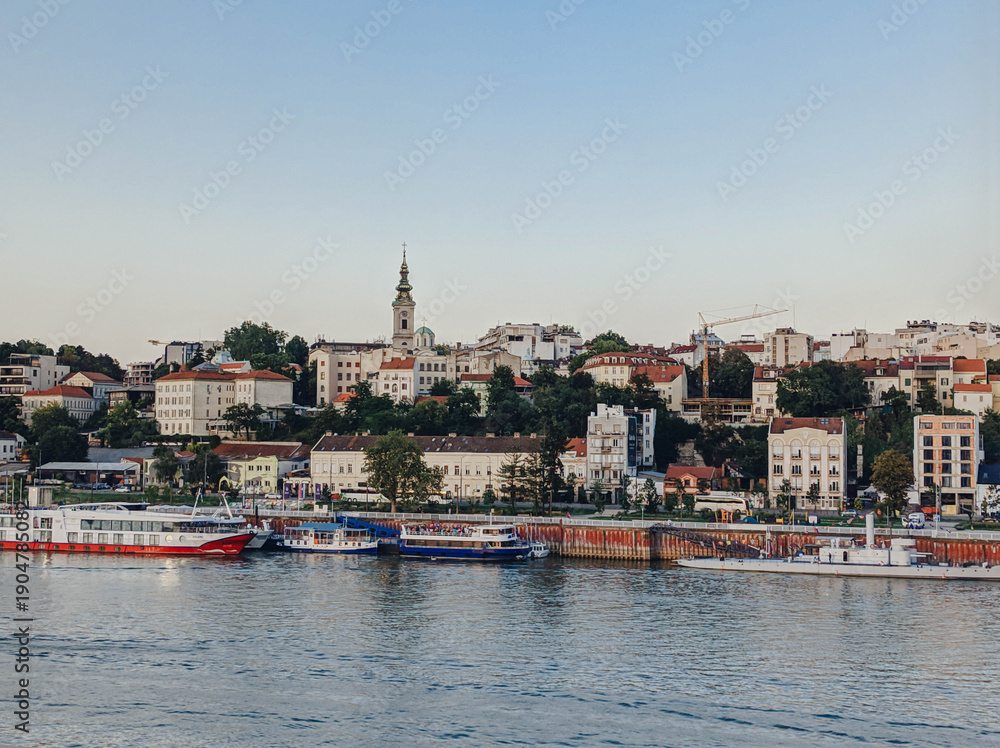 Fototapeta premium View of Belgrade city center from the Sava river with historic buildings, church tower and waterfront boats. European urban skyline with soft vintage tones