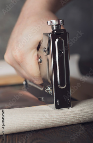 Staple gun stretching canvas on wooden frame by hand