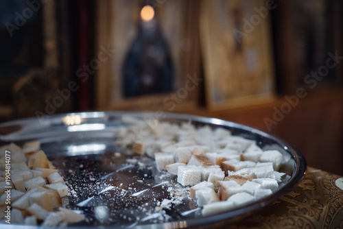 Consecrated bread antidoron on shiny silver platter close-up, against blurred icons in Orthodox church