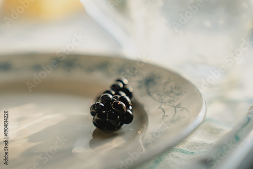 Black ripe blackberry on white plate in summer sun, blurred light and shadow