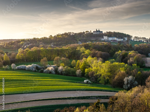 Malowniczy widok na Górę św. Anny w województwie opolskim. Wiosenny krajobraz z zielonymi polami, kwitnącymi drzewami i bazyliką na wzgórzu o zachodzie słońca. Perła Opolszczyzny.