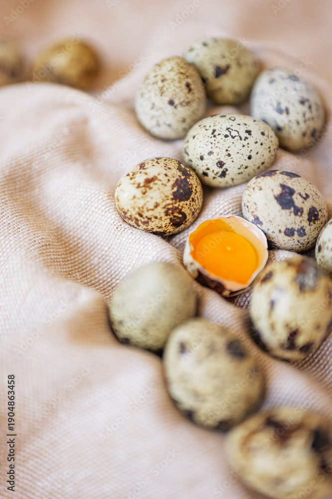 Obraz premium Quail eggs and one cracked egg with yolk on soft surface in simple setting