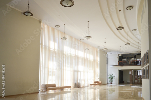 Принти на полотні Spacious modern hall interior with tall sheer curtains, curved ceiling design, hanging lights, and polished floor reflecting natural sunlight
