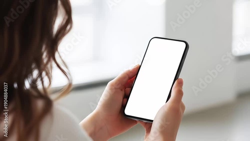 Hand holding mobile smartphone with blank white screen mockup in bright minimalist office background for app design website display copy space branding marketing ui ux presentation.
