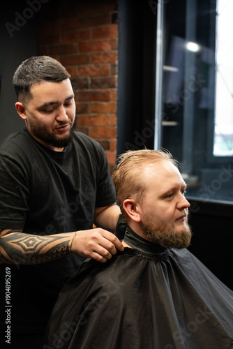 Wallpaper Mural A barber trims a client's hair in a modern barber shop with exposed brick walls and a large window. The barber wears black clothing and has a geometric tattoo on his forearm.  Torontodigital.ca