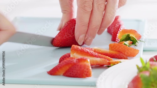 Woman slices strawberries on a cutting board using a knife with a pink handle. High quality 4k footage