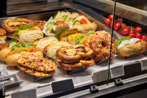Fotografija Variety of ready-to-eat sandwiches, bread rolls, pretzels, and pastries arranged in a refrigerated food display