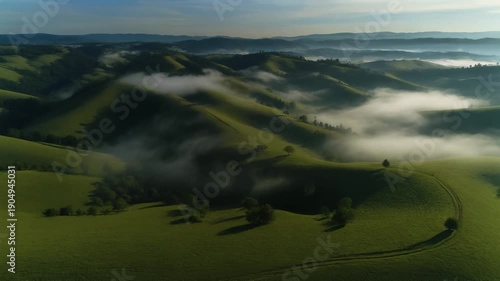 Aerial shot over rolling green hills with scattered mist