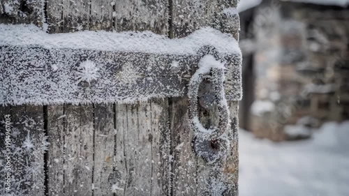 Snowcovered timber gatehouse door partially open sharp focus on frost details on wood with blurred snowdusted gatehouse walls in the background.