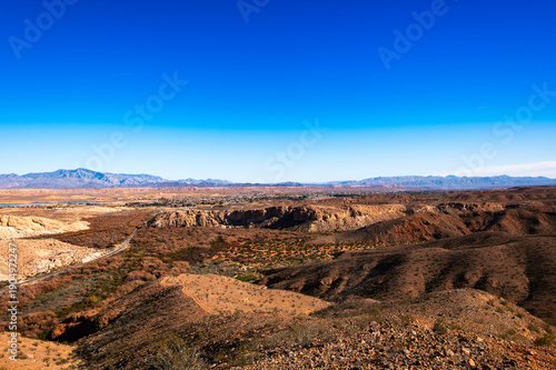 Vast desert canyon panorama with rust-red mesas and rolling arid ridges under a vivid cobalt sky, offering expansive horizons and stark geological textures.