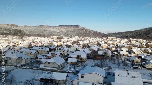 Houses in a village near snow-covered mountains with pine trees in winter. Aerial panoramic drone view from above, top view from drone.  Ukraine, Carpathians, Skole city
