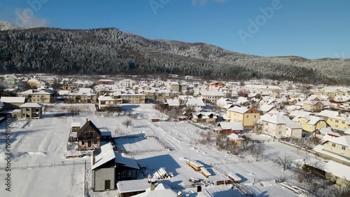 Aerial drone view of houses in a village near snow-covered mountains with pine trees in winter. Aerial panoramic drone view from above, top view from drone.  Ukraine, Carpathians, Skole city
