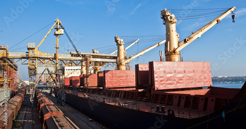 Industrial port terminal loading a cargo ship with heavy cranes and freight trains