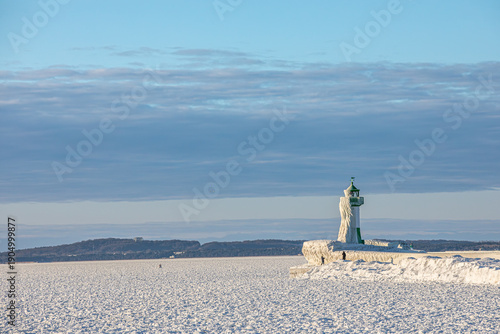 Eisverkrusteter Leuchtturm mit Eiszapfen an der vereisten Mole im Hafen von Sassnitz auf Rügen, zugefrorene Ostsee bei extremer Kälte, Wolkenbänder und viel Textfreiraum