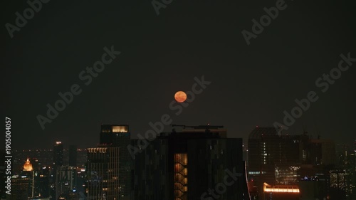 Luminous blood moon seta over modern Bangkok cityscape at night with illuminated skyscrapers rooftops and city lights