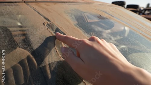 Hand touching a car windshield with a reflection.
