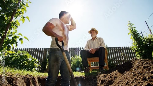 Man digging in garden with elderly man watching.