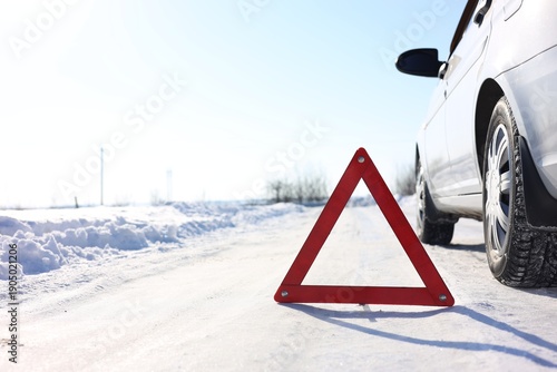 Fotografi Warning triangle and broken car on roadside at snowy winter, space for text