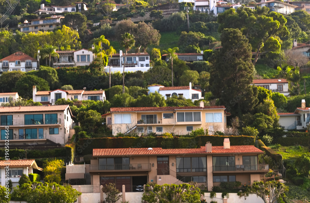 Fototapeta premium Hillside homes overlook Torrance Beach, California, showcasing Mediterranean architecture, dense greenery, and sunlit coastal living.