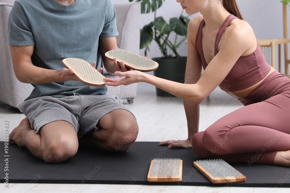 © New Africa - Young man and woman with sadhu boards on yoga mat at home, closeup