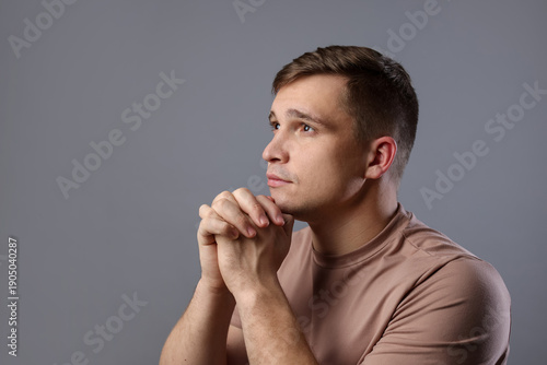 Young man praying on light grey background, space for text