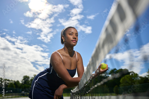 Beautiful African-American Woman playing tennis - blue dress leaning on net - shot from low vantage sky in background