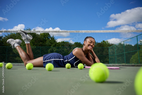 Beautiful African-American Woman playing tennis - blue dress laying down on court near net - out of focus balls in foreground