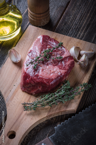 Raw ribeye steak with garlic and thyme on a wooden board, top view.