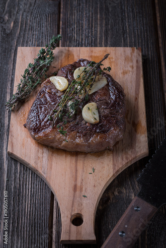 Grilled ribeye steak with garlic and thyme on a wooden table, top view.