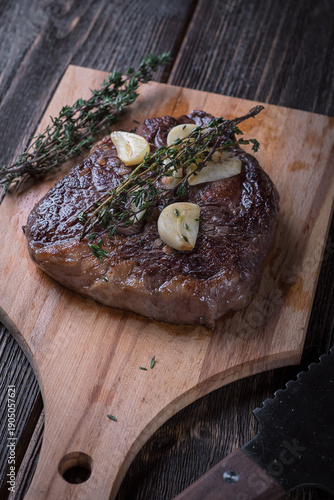 Grilled ribeye steak with garlic and thyme on a wooden table, top view.