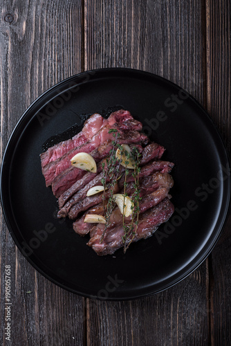 Grilled rib eye steak cut on black plate on wooden table, top view.