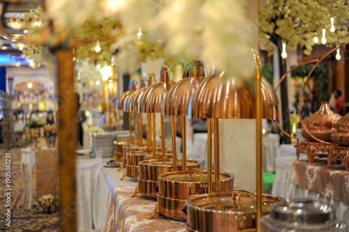 Elegant row of copper heat lamps and chafing dishes on buffet table in banquet hall. Premium catering setup for hotel, wedding reception, and hospitality food service