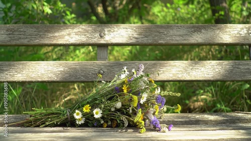 Flowers rest on an old weathered wooden bench with greenery visible in the background