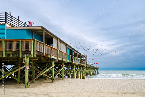 Photos Sea birds fly above the wooden Pier 14 along the Grand Strand sandy beach of the Atlantic Ocean at Myrtle Beach, South Carolina