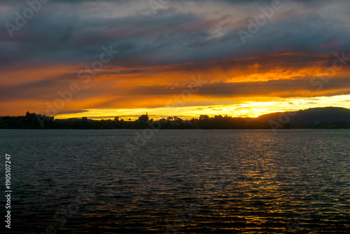 Canvas Print A suns golden sliver between dark moody sky and rippled surface of bay