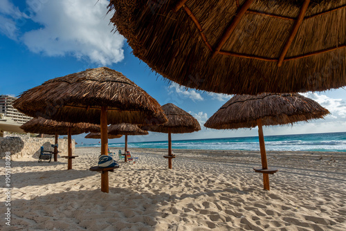 Canvastavla Sombrillas de palapa sobre arena blanca frente al mar Caribe con el sol brillando entre las nubes