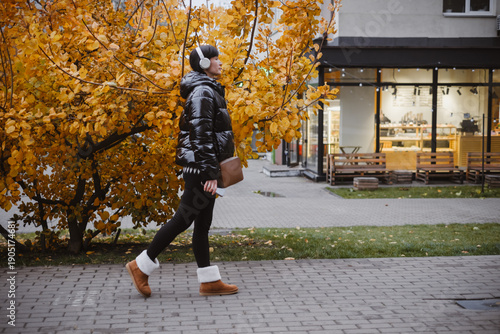 Woman wearing headphones is consciously walking through an autumn city courtyard, listening to music and maintaining her mental health.